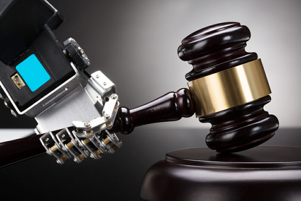 Close-up Of A Robot's Hand Striking Gavel On Sounding Block Against Grey Background