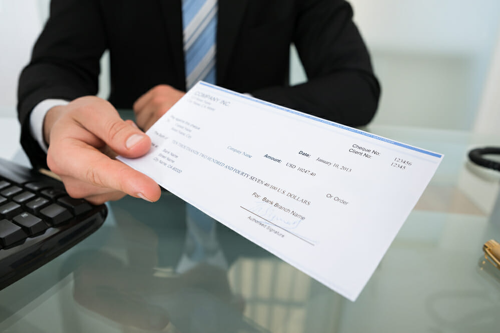 Midsection of businessman giving cheque at desk in office