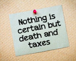 Nothing is certain but death and taxes Message. Recycled paper note pinned on cork board. Concept Image